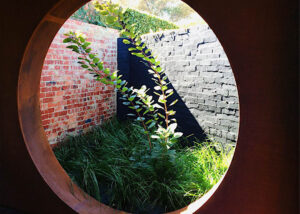 Circular window opening framing garden view with brick walls and native plantings in Brighton East courtyard