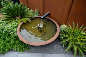 Circular copper-rimmed water feature with black spout surrounded by tropical plantings in Brighton East courtyard