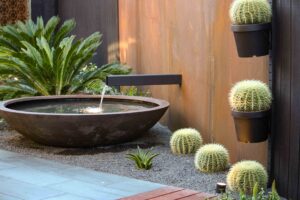 Modern courtyard with circular black water bowl, corten steel spout, and vertical cactus planters in Brighton East