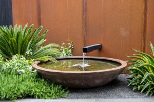 Circular concrete water feature bowl with spout against corten steel wall in Brighton East modern courtyard garden