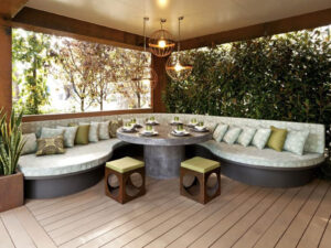 Curved concrete banquette seating with cushions around circular dining table in covered outdoor area, Melbourne