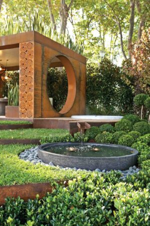 Circular water feature with corten steel moon gate structure in landscaped garden setting