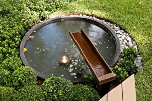 Round water feature with timber spout surrounded by river stones and native plantings in Melbourne show garden
