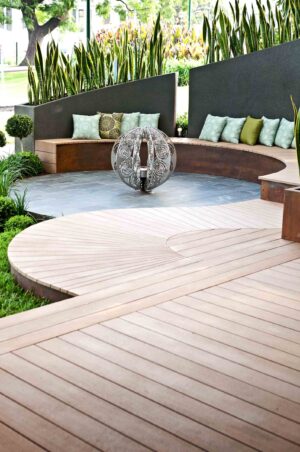 Curved timber decking with built-in bench seating, decorative water feature and contemporary planters at Melbourne show garden