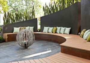 Curved timber bench seating with green cushions around decorative water feature in contemporary Melbourne show garden