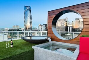 Circular timber screen with city views on 10-storey Docklands rooftop featuring hot tub and artificial turf