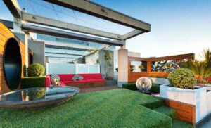 Modern rooftop garden with glass pergola, red seating, artificial turf and city views in Docklands Melbourne