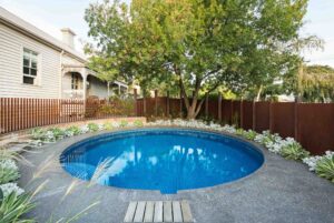 Round swimming pool with blue mosaic tiles and corten steel surround, landscaped with succulents and established tree