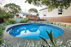 Round swimming pool with blue mosaic tiles surrounded by corten steel edging and timber screening in modern Hawthorn backyard