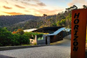 Modern concrete and timber home nestled in coastal bushland at sunset with vertical corten steel entry signage, Separation Creek