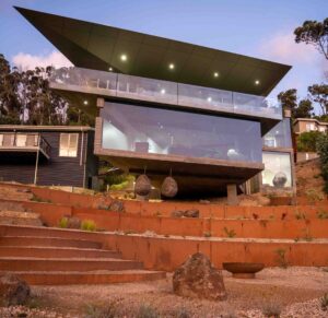 Tiered corten steel retaining walls with gravel paths leading to modern coastal home with cantilevered roof at Separation Creek
