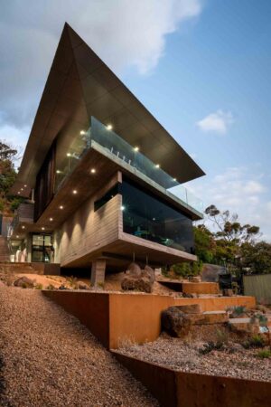 Tiered corten steel terraces step down steep coastal site beneath modern home with green roof at Separation Creek