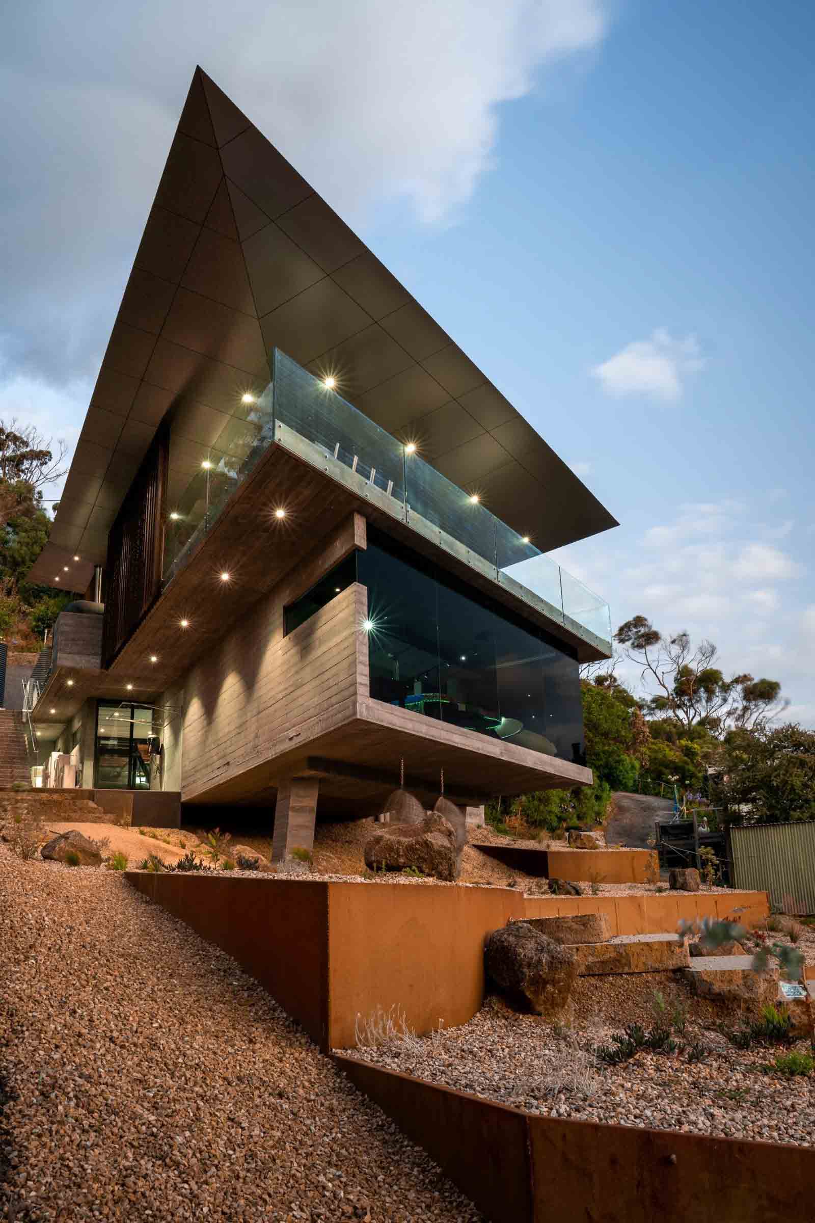 Tiered corten steel terraces step down steep coastal site beneath modern home with green roof at Separation Creek
