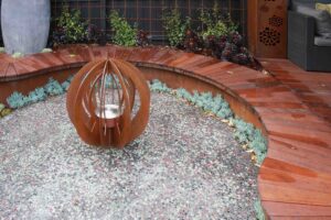 Rusted corten steel bottle tree sculpture surrounded by circular concrete aggregate and curved timber bench seating in Malvern East