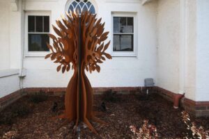 Corten steel bottle tree sculpture in mulched garden bed at Malvern East family home with white rendered walls