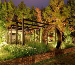 Circular brick moon gate archway with steel pergola and autumn trees lit at dusk in award-winning Mandala Garden, Nagasaki