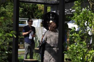 Two people conducting interview in garden setting with moon gate structure visible, Mandala Moon Gate Garden Nagasaki