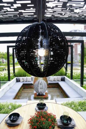 Black perforated circular moon gate sculpture suspended above sunken seating area at Mandala Garden, Nagasaki Japan