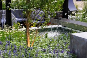 Stainless steel water spout flowing into tiled pool with moon gate and mixed plantings at Nagasaki garden show