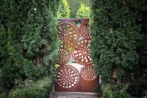 Decorative corten steel garden gate with circular perforations framed by established evergreen hedging in Mt Eliza
