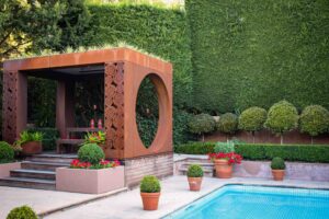 Corten steel pavilion with geometric screening beside swimming pool in Mt Eliza formal garden with hedge backdrop