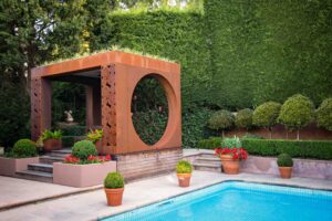 Modern corten steel pavilion with circular opening beside swimming pool in Mt Eliza formal garden setting