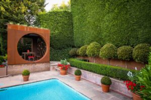 Circular corten steel pavilion beside swimming pool with formal hedge backdrop and topiary plantings at Mt Eliza residence