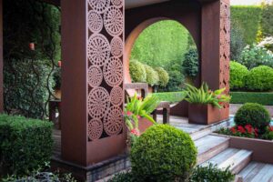 Corten steel pavilion with perforated screens and circular opening framing formal garden hedging in Mt Eliza