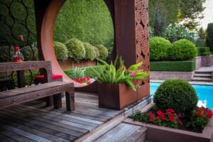 Corten steel pavilion with decorative screens and timber decking beside formal hedged garden and pool in Mt Eliza
