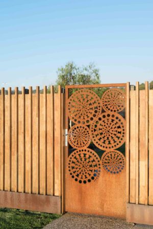 Custom corten steel gate with circular perforated patterns in timber fence at Buninyong corner block residence