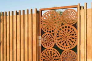 Custom corten steel garden gate with circular perforated pattern in timber fence frame at Buninyong residence