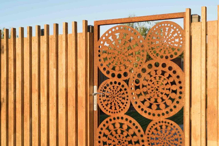 Custom corten steel garden gate with circular perforated pattern in timber fence frame at Buninyong residence