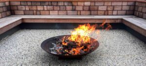 Circular steel fire pit with timber bench seating on aggregate surface in modern native garden, Buninyong residence