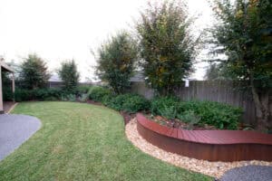 Curved Corten steel garden edging separating lawn and planting beds with concealed drainage detailing in Ballarat residential landscape.