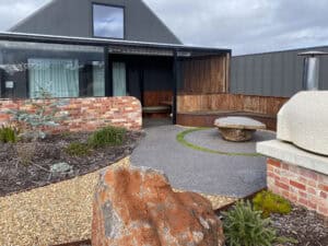 Curved brick feature wall, exposed aggregate path, and built-in timber seating at Gisborne residence courtyard.