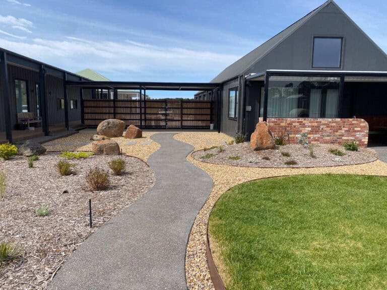 Curved exposed aggregate path wrapping around lawn and planting beds at Gisborne residence.