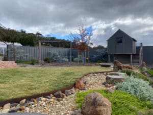 Expansive lawn bordered by curved corten edging, gravel swale, and boulders at Gisborne property.
