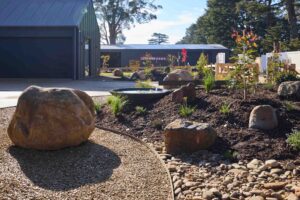 Large basalt boulders positioned throughout native garden beds with gravel paths and modern house backdrop in Daylesford