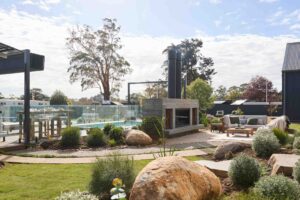 Modern concrete outdoor fireplace with glass pool fencing and mature plantings at Daylesford House 5 from The Block