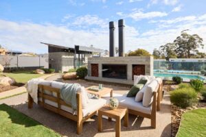 Concrete outdoor fireplace with timber furniture and swimming pool at Daylesford House 5 from The Block television show