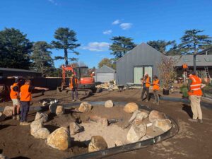 Construction workers in high-vis orange installing landscape features with excavator and boulders at Daylesford site