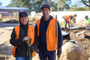 Two landscape construction workers in orange safety vests and caps posing with tools on The Block Daylesford project site