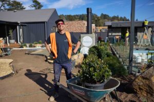 Landscaper in hi-vis vest and sunglasses with wheelbarrow full of plants during The Block Daylesford construction