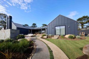 Modern landscape with curved aggregate paths, native plantings and dark metal clad house at Daylesford House 5