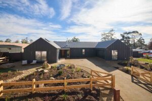 Modern black house with integrated Pickleball court, mature Bottle Tree and curved garden beds in Daylesford