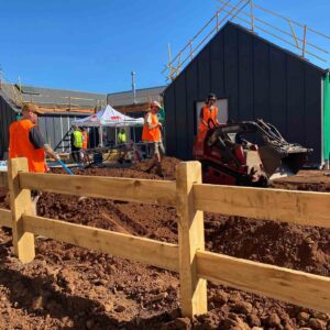 Construction workers in high-vis using mini excavator with timber boxing frames for concrete footings at Daylesford site