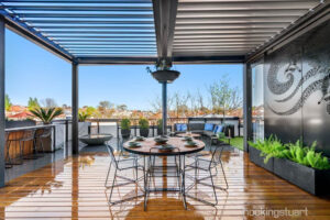 Modern rooftop terrace with blackbutt timber decking, round dining table, wire chairs and pergola overlooking St Kilda