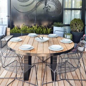 Round blackbutt timber dining table with wire chairs on St Kilda rooftop terrace with planters and city views