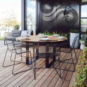Round blackbutt timber dining table with black metal chairs on timber deck terrace overlooking St Kilda