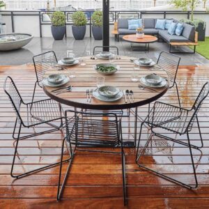 Round timber dining table with black wire chairs set for six people on wooden deck, St Kilda rooftop terrace